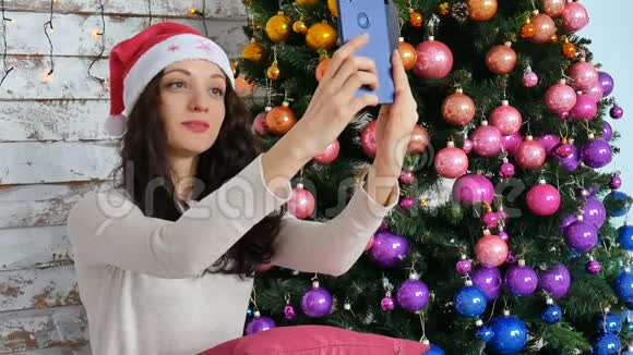 一个戴圣诞帽的女孩正在一棵新年树附近拍照创意圣诞设计视频的预览图