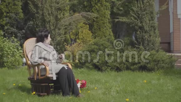 肖像成熟的女士坐在摇椅上享受阳光成年孙子带着水缸来视频的预览图