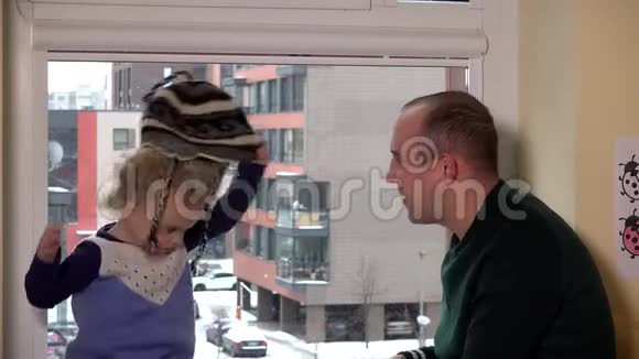 带孩子的人在窗户附近测量温暖的冬帽暴风雪视频的预览图