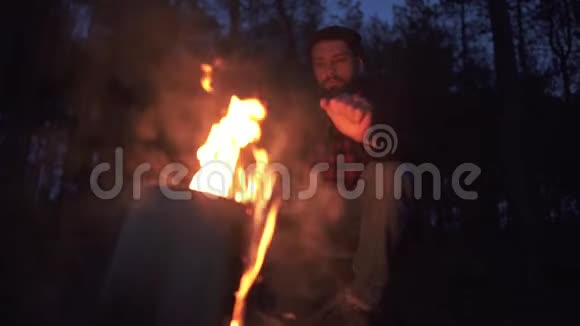 一个有珠的人坐在篝火旁在黑暗中举起双手在森林里取暖森林里火堆旁的伐木工人视频的预览图
