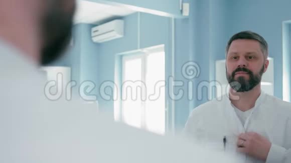 快乐的医生正在准备工作并在镜子附近穿上他的实验室外套视频的预览图