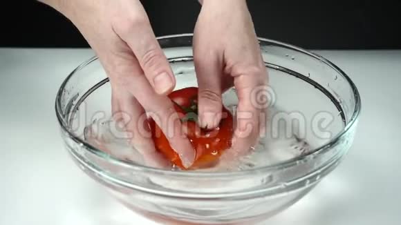 女性双手洗一个成熟的红番茄放在一碗白色背景的清水中慢动作视频的预览图