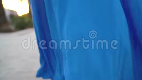 女人穿着一件漂亮的蓝色连衣裙沿着棕榈大道走从后面看慢动作视频的预览图