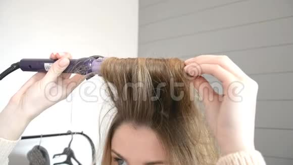 在美容室用发钳卷发的年轻金发女子的肖像视频的预览图