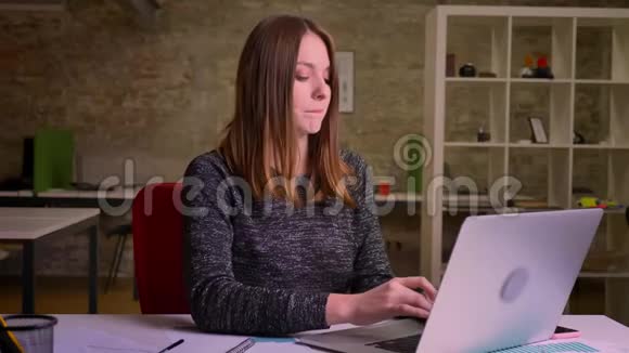 红头发的女商人在座位上跳舞同时用笔记本电脑打字视频的预览图