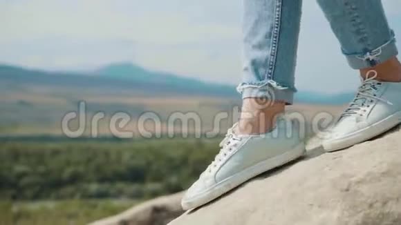 孤独的人与自然拍摄近腿的女孩穿着白色运动鞋和短牛仔裤女士坐在岩石上视频的预览图