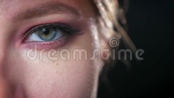 特写蓝绿色的眼睛有着令人敬畏的彩色眼影的白种人女孩看着相机的寒冷黑暗的背景视频的预览图