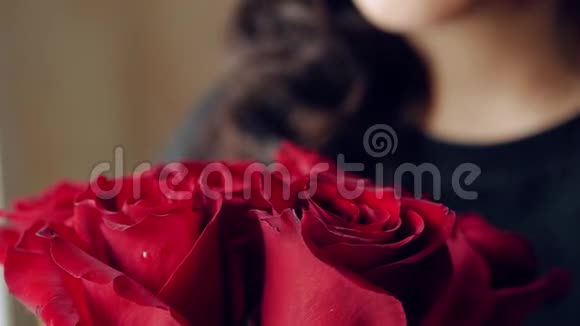 美丽的女孩嗅着一束红玫瑰然后看着窗外特写视频的预览图