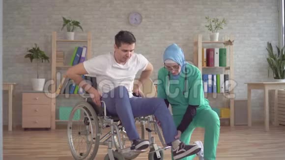 戴头巾的穆斯林护士帮助残疾人从轮椅上站起来视频的预览图