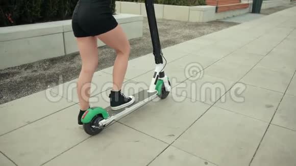 穿着黑色衣服和运动鞋的女孩骑着电动滑板车在城市里转悠视频的预览图