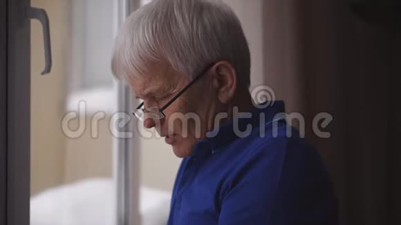 孤独的老人戴着眼镜站在窗边视频的预览图