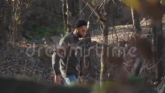 一个人手拿斧子走在森林里一个留胡子的年轻人拿着斧头在户外散步视频的预览图