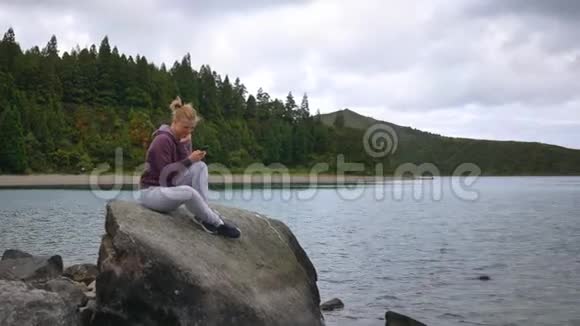 女孩在湖和湖的背景下看智能手机玩得很开心视频的预览图