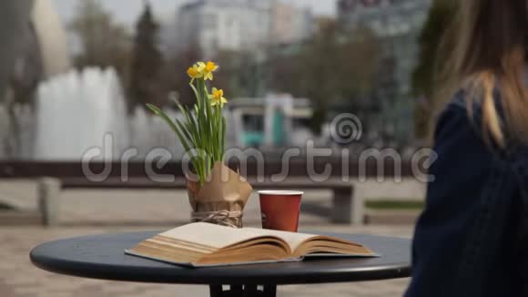 年轻女子喝着咖啡读着一本书在一个俯瞰喷泉的咖啡馆的桌子上翻阅着书页视频的预览图