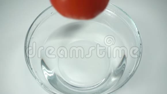 一个成熟的红番茄掉进玻璃碗里喷水慢动作白色背景清水中的大番茄视频的预览图