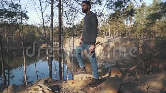 容人拿着斧子站在山上眺望着一片令人惊叹的湖泊和森林一个有斧头的人站在悬崖上视频的预览图