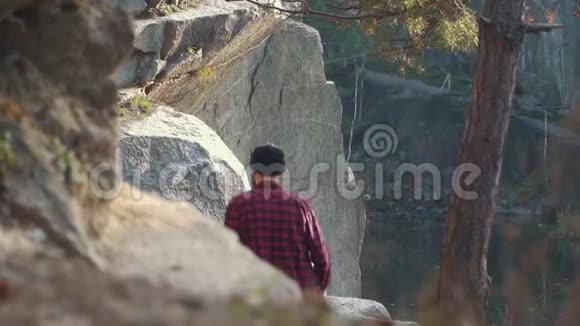戴着帽子和格子衬衫的人爬上悬崖附近的石头在户外散步的人视频的预览图