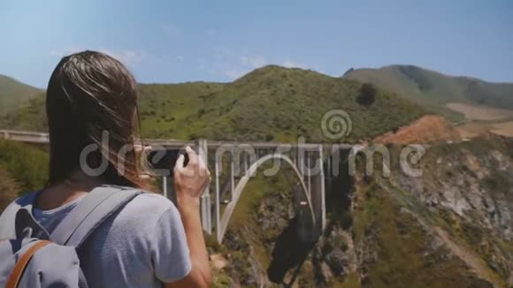 带背包的年轻游客女士在标志性的比克斯比峡谷大桥大苏尔拍智能手机史诗般的风景视频的预览图