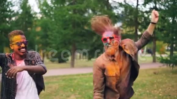 在公园的霍利节上戴着墨镜脸上画着画的年轻人在户外跳舞和大笑视频的预览图