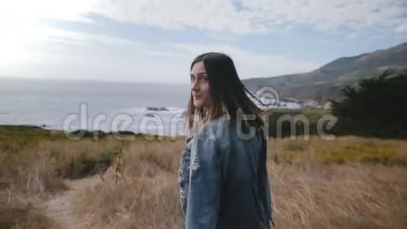 镜头跟随年轻快乐的女人在黄花和干燥的植被中徒步旅行回首大苏尔海海岸线视频的预览图