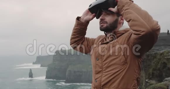 一个年轻的玩具在悬崖顶上玩VR的肖像有着惊人的景观他穿着VR给人留下了很深的印象视频的预览图