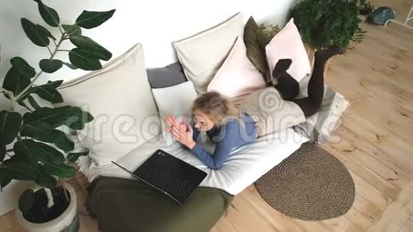 美丽开朗的女人带着笔记本电脑躺在沙发上笑得很开心视频的预览图