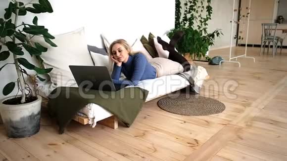 美丽开朗的女人带着笔记本电脑躺在沙发上笑得很开心视频的预览图