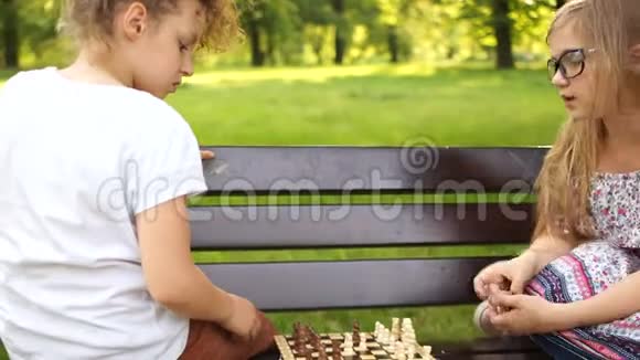 暑假智力游戏两个十几岁的女孩在公园里坐在长凳上下棋视频的预览图