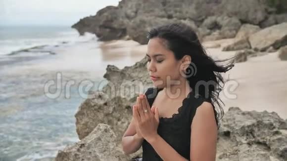 印度尼西亚女孩在多岩石的巴厘岛海滩上祈祷视频的预览图