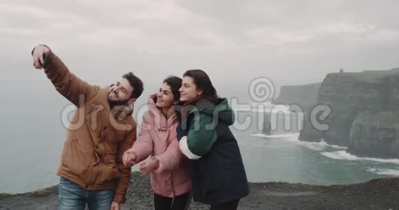 快乐的三个朋友在悬崖顶上用智能手机拍照留念多元民族就在视频的预览图
