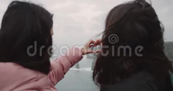 悬崖顶上的两个女游客的详细情况令人高兴地看着海景双手捧起一颗大心脏视频的预览图
