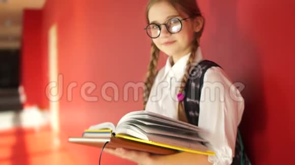 漂亮的女学生手里拿着眼镜和书看着镜框微笑着回到学校视频的预览图