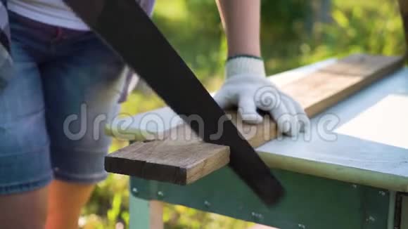 戴防护手套的女性手在外面锯木板视频的预览图