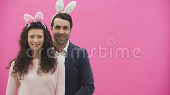 年轻夫妇站在粉红色的背景上在此期间手势课露出微笑看着镜头快乐视频的预览图