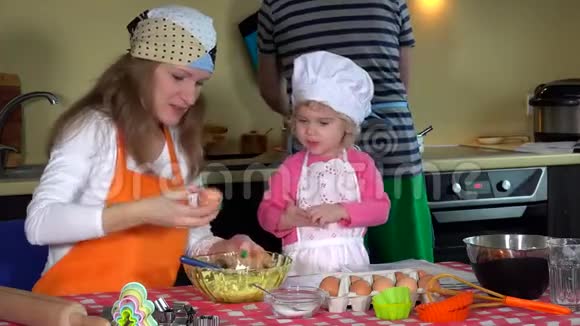 可爱的父母带着可爱的学步女孩带着厨师帽准备厨房饼干视频的预览图