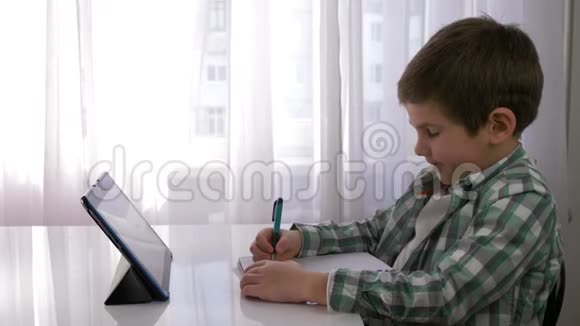 儿童教育可爱的小男孩使用平板电脑进行家庭教育并在笔记本上做笔记坐在房间的桌子上视频的预览图