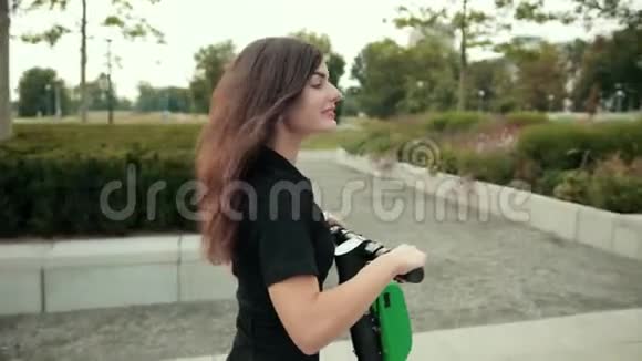 穿着黑色衣服和运动鞋的女孩骑着电动滑板车在城市里转悠视频的预览图