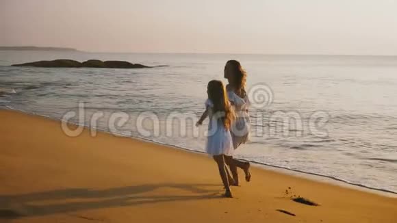 快乐美丽的年轻母亲和小女儿一起玩耍和旋转在史诗般的日落海洋海滩上玩得开心视频的预览图