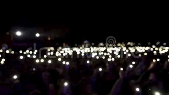 观众在大厅中分散注意力灯光在黑暗中挥动行动观众手持带有闪亮手电筒的手机视频的预览图