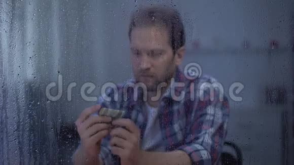中年男子在雨窗后数钱预算差贫穷视频的预览图
