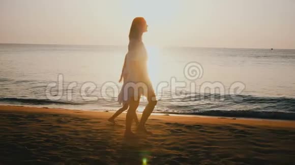 幸福美丽的年轻母亲和小女儿携手漫步在史诗般的热带日落海滨度假胜地视频的预览图
