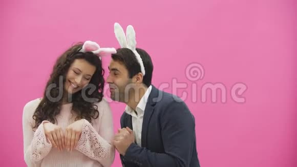 漂亮的年轻夫妇站在粉红色的背景上在此期间他们重新创造了野兔的运动放置视频的预览图