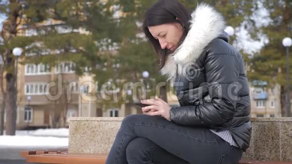 在一个城市公园里坐在长凳上打电话的开朗女人视频的预览图