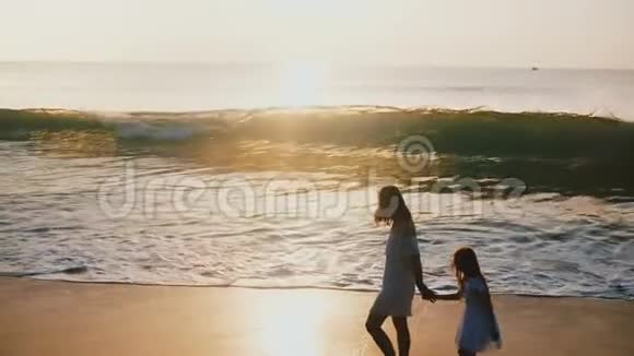 快乐的中年母亲和小女儿一起逃离大浪在史诗般的日落海滩上玩得很开心视频的预览图
