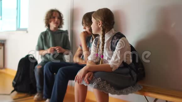 一群带背包的学童坐在学校走廊的木凳上回学校去青少年打招呼视频的预览图