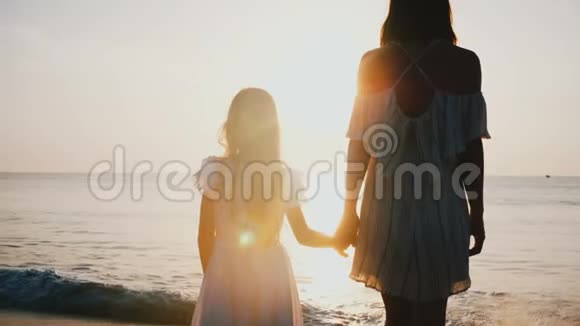 年轻的母亲和小女儿手牵着手在不可思议的海滩上观看史诗般的日落视频的预览图