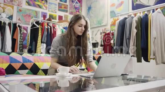 年轻女子一边喝咖啡一边工作一边用笔记本电脑视频的预览图