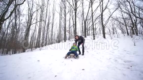 一个家庭冬季的周末小男孩迅速滑下雪橇从白雪覆盖的山脉视频的预览图