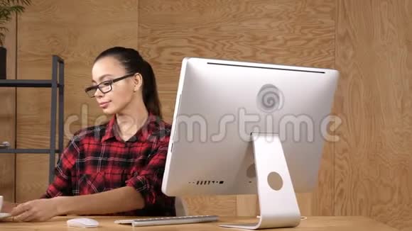 偶然的女人在电脑前的现代办公室里喝咖啡视频的预览图