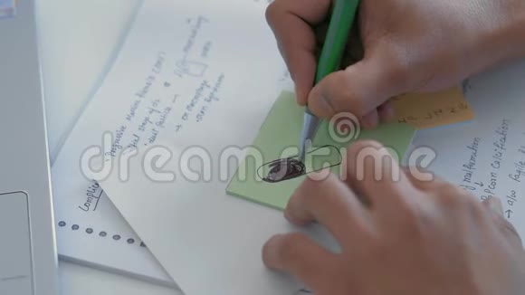 特写印度学生的手在贴纸上画了一块平板电脑提醒人们即将到来的医学考试视频的预览图